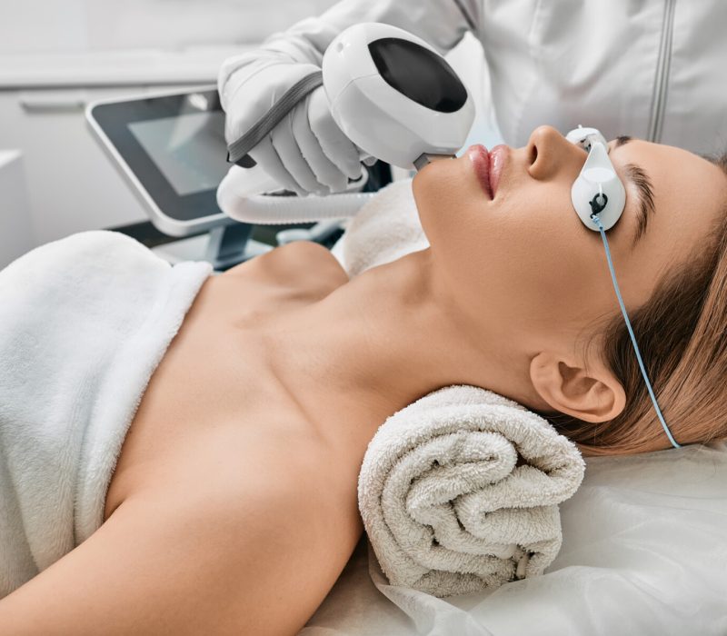 Photorejuvenation, rosacea treatment, removing brown spots and vascular mesh. Cosmetologist using IPL apparatus treats skin of female patient's face